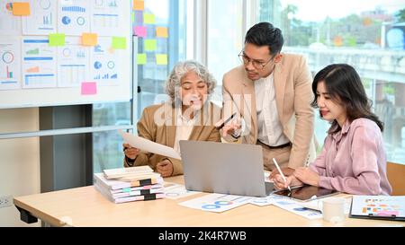 Homme d'affaires ou chef d'équipe asiatique élégant et séduisant regardant l'écran d'un ordinateur portable, brainstorming et analyse du plan financier avec son équipe lors de la réunion. Banque D'Images