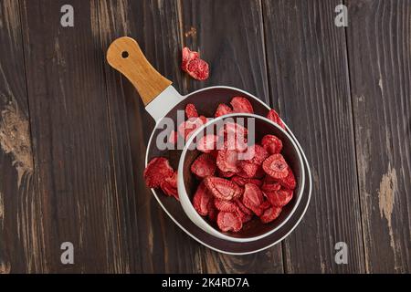 Les copeaux de fraise sont empilés dans un plat en céramique avec une poignée en bois sur fond de béton gris-bleu. 100 % de fraises lyophilisées naturelles Banque D'Images