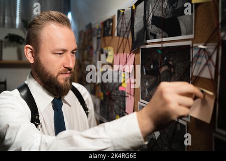 Détective regardant le tableau avec des empreintes digitales, des photos, une carte et des indices reliés par une ficelle rouge sur le mur, travaillant au bureau Banque D'Images