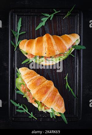 Croissants au saumon salé, au concombre et à l'arugula servis sur fond sombre. Gros plan. Vue de dessus Banque D'Images