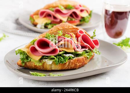 Croissant frais ou sandwich avec salade, jambon et fromage sur fond clair. Banque D'Images