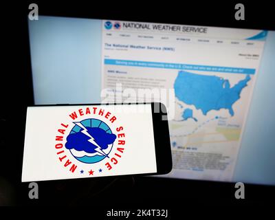 Personne tenant un téléphone portable avec le logo de l'agence américaine National Weather Service (NWS) sur l'écran devant la page Web. Mise au point sur l'affichage du téléphone. Banque D'Images