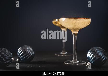 Champagne du nouvel an festif dans des verres à vin décorés de boules bleues de Noël sur fond noir. Gros plan. Carte de vœux de fin d'année avec espace de copie. Banque D'Images