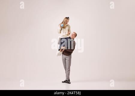 Jeune homme de style rétro vêtements d'hiver tenant une fille tendre sur ses épaules isolée sur fond gris. Vacances, bonheur, amour concept Banque D'Images