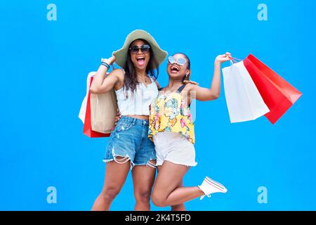 Portrait de deux jeunes femmes heureuses vêtues de vêtements d'été tenant des sacs de shopping isolés sur fond bleu, appréciant le Vendredi fou. Gaiement Banque D'Images