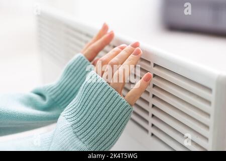 Main de femme sur un radiateur blanc. Saison de chauffage. Crise énergétique. Batteries froides. Chauffage central Banque D'Images