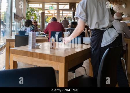 Un ouvrier de cuisine qui débarque des tables dans un restaurant animé de Newquay, en Cornouailles, au Royaume-Uni. Banque D'Images