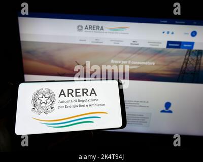 Personne tenant un smartphone avec le logo de l'autorité de régulation italienne ARERA sur l'écran devant le site. Mise au point sur l'affichage du téléphone. Banque D'Images