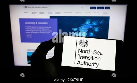 Personne tenant un téléphone portable avec le logo de l'autorité de transition de la mer du Nord britannique (NSTA) à l'écran en face de la page Web. Mise au point sur l'affichage du téléphone. Banque D'Images