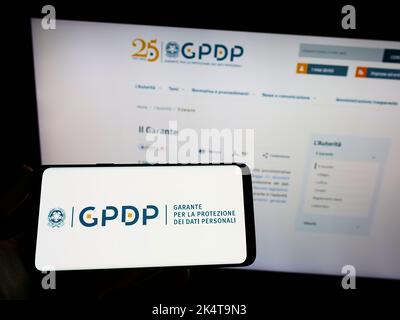 Personne portant un smartphone avec le logo de l'autorité italienne de protection des données (GPDP) à l'écran devant le site Web. Mise au point sur l'affichage du téléphone. Banque D'Images