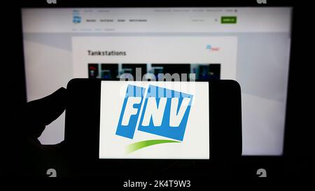 Personne tenant un téléphone portable avec le logo du néerlandais Federatie Nederlandse Vakbeweging (FNV) à l'écran devant la page Web. Mise au point sur l'affichage du téléphone. Banque D'Images