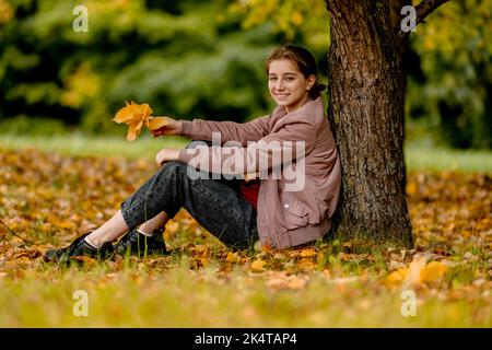 Une adolescente est assise dans un parc d'automne Banque D'Images