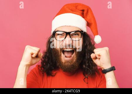 Gros plan d'un barbu portant un chapeau de père noël et criant à l'appareil photo. Banque D'Images