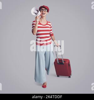 Heureuse voyageur femme avec sa valise, elle crie à travers un mégaphone Banque D'Images