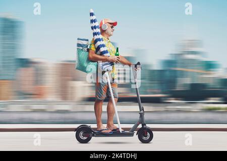 Heureux touriste senior à cheval un scooter électrique écologique et aller à la plage, ville en arrière-plan Banque D'Images