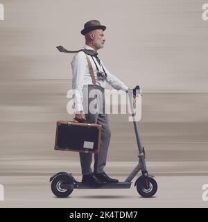 Homme de style vintage portant une valise et portant un scooter électrique, il est un voyageur et un photographe Banque D'Images