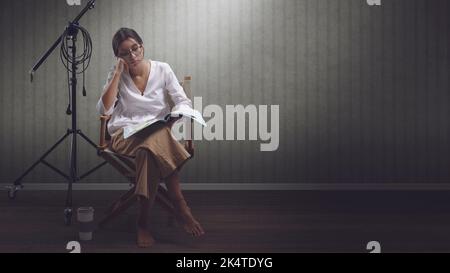 Actrice professionnelle concentrée assise sur la chaise du réalisateur et lisant un script de jeu, espace de copie vierge Banque D'Images