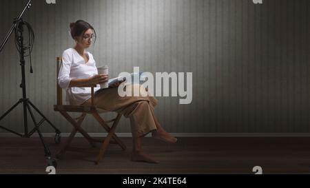 Actrice professionnelle concentrée assise sur la chaise du réalisateur et lisant un script de jeu, espace de copie vierge Banque D'Images