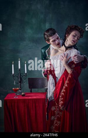 Portrait du jeune homme à l'image du prince médiéval, vampire mordant la jeune femme innocente sur fond vert foncé. Boire du sang Banque D'Images