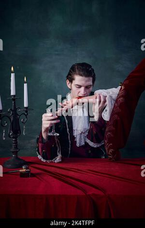 Portrait d'un jeune homme sans fin à l'image d'un vampire qui boit du sang de la main de la femme sur fond vert foncé Banque D'Images