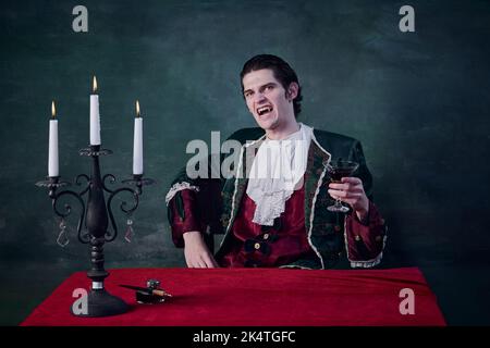 Portrait d'un homme terrifiant à l'image du vampire, verre de sang levant Dracula sur fond vert foncé. Grinçant Banque D'Images