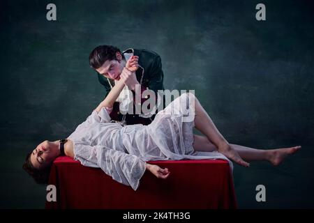 Portrait de l'homme à l'image de la main vampire de la jeune femme couché sur une table sur fond vert. Boire du sang Banque D'Images