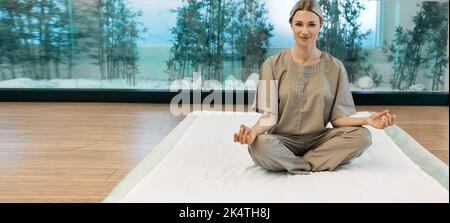Yoga, méditation, exercices de respiration. Belle femme assise dans lotus poser sur le tapis de yoga et se détendre dans la confortable salle de méditation Banque D'Images