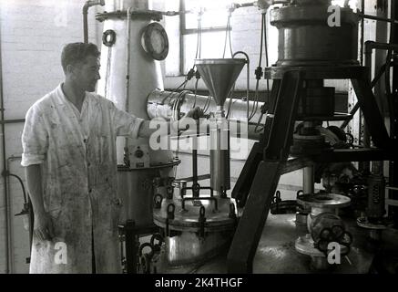 Années 1960, historique, un ouvrier masculin en salopette sale vérifiant une valeur à l'intérieur d'une unité industrielle dans une petite entreprise de fabrication de peinture, Angleterre, Royaume-Uni. Banque D'Images