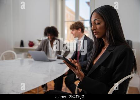 Une femme d'affaires africaine au bureau utilise sa tablette tandis que ses collègues travaillent en arrière-plan, concept de bureau Banque D'Images