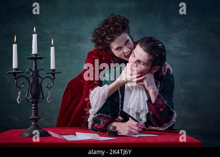 Portrait d'un jeune homme qui écrit une lettre et d'une femme à l'image d'un vampire qui mord son cou sur fond vert foncé Banque D'Images