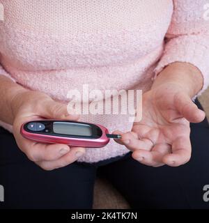 Femme âgée vérifiant le taux de sucre dans le sang à l'aide d'un glucomètre. Gros plan main de la personne âgée avec le diabète. Traitement du diabète chez les personnes âgées. Banque D'Images
