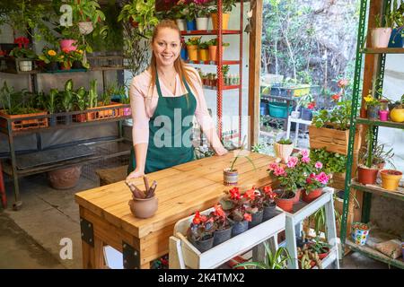 Jeune femme sympathique travaillant comme fleuriste et spécialiste commercial dans la boutique de fleurs de la pépinière Banque D'Images