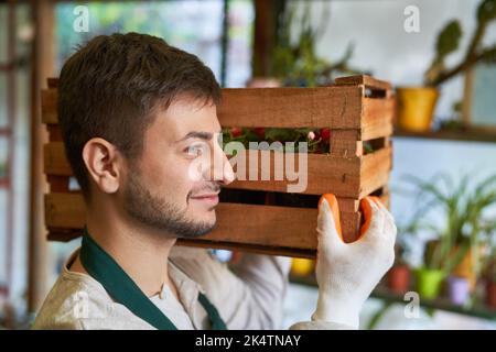 L'apprenti jeune jardinier porte une boîte de fleurs à la pépinière pour une livraison Banque D'Images