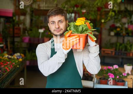 Le jeune jardinier ou fleuriste porte un pot de fleurs pour une livraison ou une commande Banque D'Images