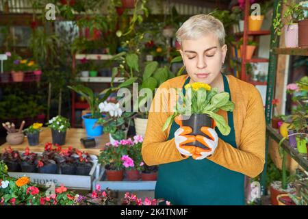 Fleuriste femme tenant une maison et appréciant le parfum dans la pépinière de fleurs magasin Banque D'Images