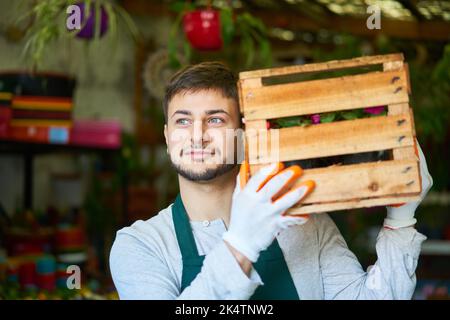 Jardinier ou fleuriste porte une boîte de fleurs pour l'expédition dans la pépinière de fleurs magasin Banque D'Images