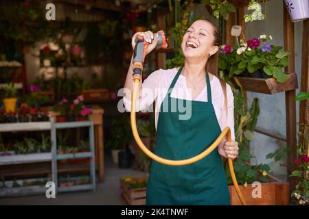 Jeune fleuriste avec tuyau de jardin chante hors de haute spiritueux et joie de vivre dans la boutique de fleurs Banque D'Images