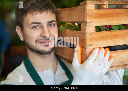 Le jeune homme en tant que jardinier porte une boîte de fleurs sur son épaule pour une livraison ou une commande Banque D'Images