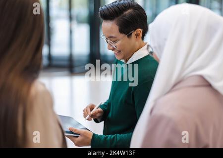 Jeune homme d'affaires montrant quelque chose à ses collègues sur une tablette au bureau Banque D'Images