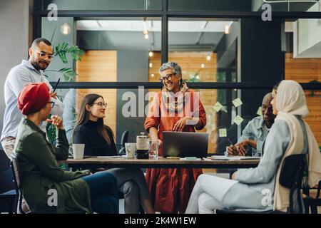 Des hommes d'affaires joyeux souriant lors d'une réunion dans un bureau créatif. Groupe de professionnels d'affaires prospères travaillant en équipe dans un multi Banque D'Images