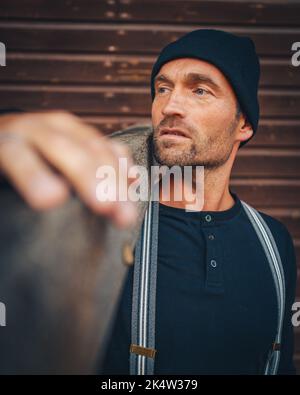 Bon homme de travail avec chapeau et bretelles porte une planche en bois Banque D'Images
