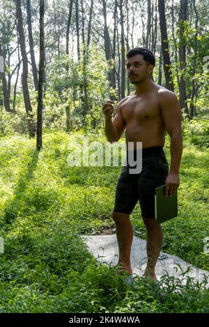 Athlète d'âge moyen mature homme debout dans des vêtements de sport sur le tapis de fitness, regardant la vidéo tutoriel d'entraînement en ligne, vlogging Banque D'Images