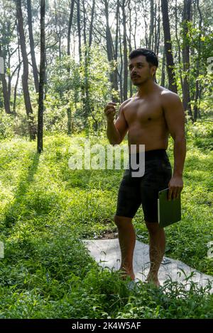 Athlète d'âge moyen mature homme debout dans des vêtements de sport sur le tapis de fitness, regardant la vidéo tutoriel d'entraînement en ligne, vlogging Banque D'Images