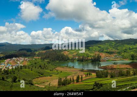 Montagnes imposantes, plantations de thé, rivière avec petites maisons visibles, ciel bleu et blanc, reflet visible dans l'eau, cadeau de la nature de verdure chaque Banque D'Images