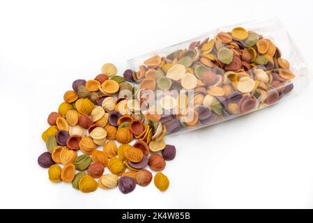 Orecchiette de pâtes colorées qui sortent d'un sac transparent, pâtes semoule de blé dur italien avec du curcuma, des épinards, de la betterave et de la carotte noire isola Banque D'Images