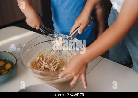Les mains des enfants font de la pâte, mélangeant des ingrédients pour un gâteau de Noël maison. Préparation de desserts à la maison. L'enfant cuisine dans la cuisine. Banque D'Images