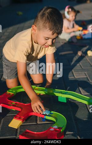 Mignon petit garçon caucasien jouant avec le chemin de fer jouet à l'aire de jeux dans l'arrière-cour. Transport ferroviaire. Éducation précoce. Banque D'Images