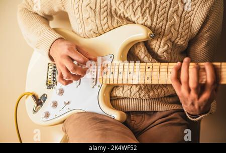 Un homme dans un pull en laine joue de la musique sur une guitare électrique blanche . Cours de musique. Créativité et inspiration. Musique rock. Banque D'Images