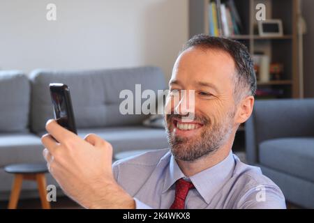 Un homme heureux utilisant un smartphone à la maison. Homme barbu portant une chemise de travail. Homme de race blanche adulte en 30s ou 40s. Banque D'Images
