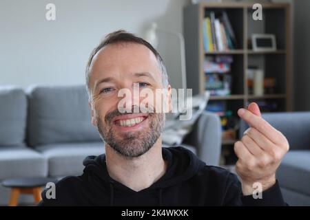 Homme souriant et montrant le style asiatique ou coréen doigt coeur geste. Homme barbu portant un pull à capuche noir décontracté. Homme caucasien adulte en 30s ou 40s souriant Banque D'Images